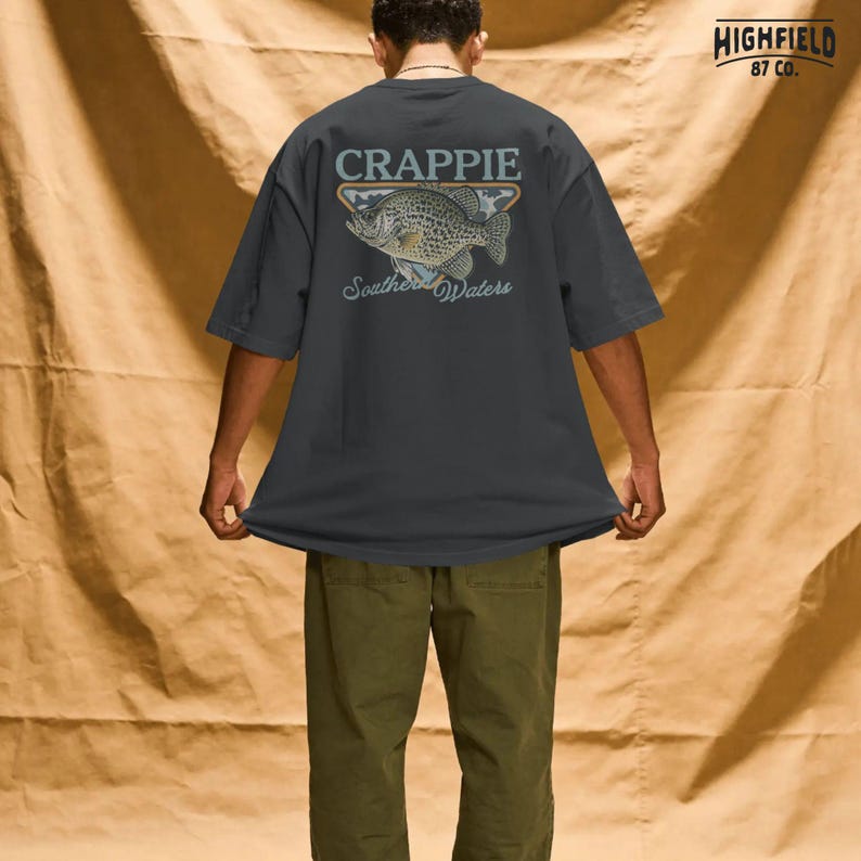 Crappie fisherman PNG showing a detailed panfish illustration with bold fish name lettering and southern fishing theme for outdoor apparel designs.