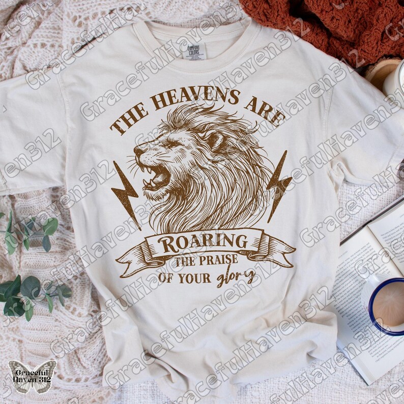 May include: A white t-shirt with a brown lion graphic and the text "The Heavens Are Roaring The Praise Of Your Glory".