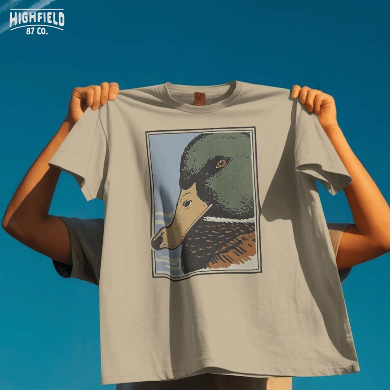 Mallard duck drake head profile artwork in a strong silhouette style with muted green and brown tones. The framed layout and clean background make it suitable for apparel graphics, duck hunting shirt designs, and waterfowl PNG digital download use for sublimation and print ready projects.