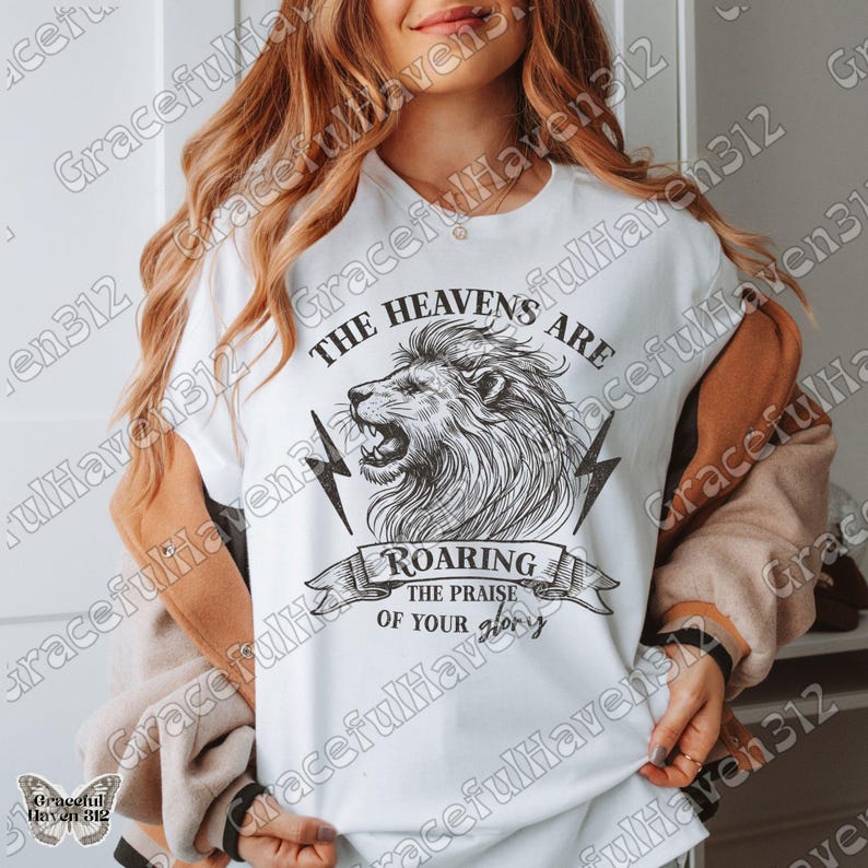 May include: White t-shirt with a black and white illustration of a lion's head roaring. The text "The Heavens Are Roaring The Praise Of Your Glory" is printed on the shirt.