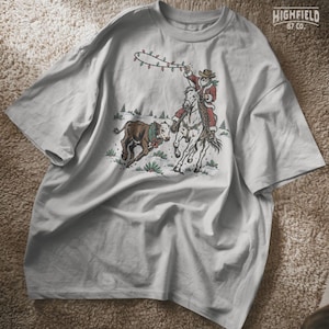 Vintage-style Western Christmas design showing Santa on horseback beside a running calf with pine trees and snowy ground in the background.
