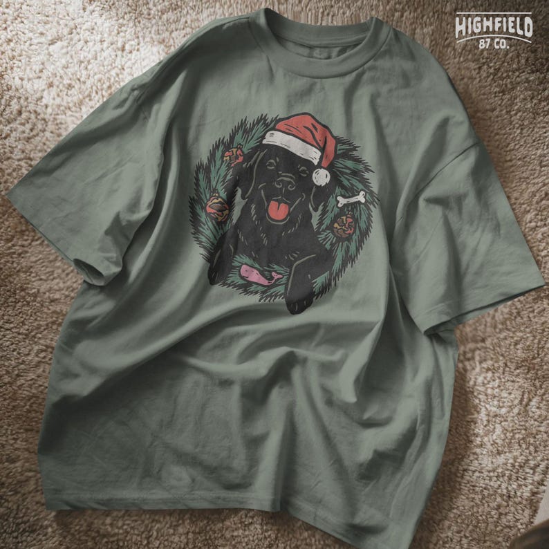 Happy black lab in Santa hat surrounded by pine leaves and holiday decor, including a bone and a pink whale toy. PNG format for seasonal crafting.