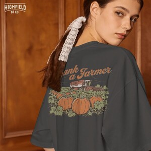 Farm shirt design showing a pumpkin patch harvest scene with a combine harvester, large pumpkins, and “Thank a Farmer” text in a vintage style agriculture illustration.