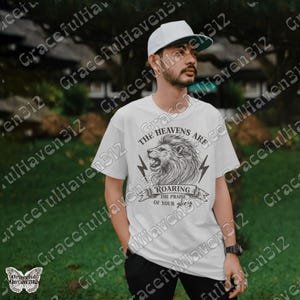 May include: White t-shirt with a black and white illustration of a lion with the text "The Heavens Are Roaring The Praise Of Your Glory".