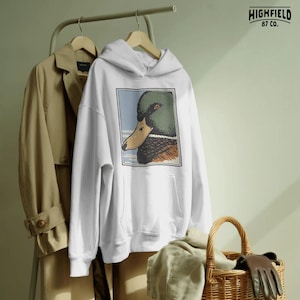 Detailed mallard duck head side view with textured plumage and expressive eye, illustrated in a vintage outdoor hunting style. The soft sky background and bordered frame enhance the clean composition. Perfect waterfowl PNG digital download for duck hunters, Father’s Day shirt designs, and outdoor wildlife apparel.