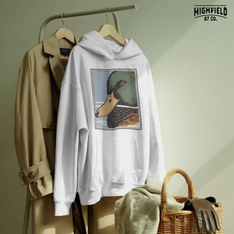 Detailed mallard duck head side view with textured plumage and expressive eye, illustrated in a vintage outdoor hunting style. The soft sky background and bordered frame enhance the clean composition. Perfect waterfowl PNG digital download for duck hunters, Father’s Day shirt designs, and outdoor wildlife apparel.