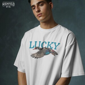 Wood duck shirt PNG with a flying waterfowl bird, colorful wing markings, red eye, black outlines, and bold Lucky typography. The artwork has a vintage outdoor feel for casual shirts, nature apparel, bird gifts, and printable digital products.