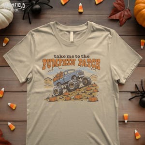 Kids autumn PNG showing a monster truck driving through a pumpkin patch with pumpkins, dirt, rocks, and fall harvest colors.