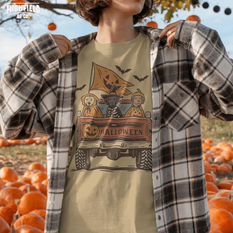 Spooky puppy costume PNG showing a vintage style pickup truck carrying three Halloween dogs with orange pumpkin accents and bat silhouettes.