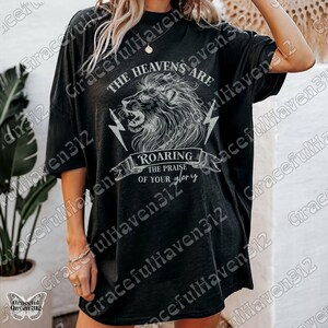 May include: Black oversized t-shirt with a white graphic of a lion roaring with lightning bolts and the text "The Heavens Are Roaring The Praise Of Your Glory".