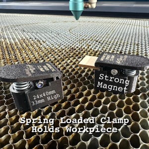 May include: Two black spring-loaded clamps with the text "Magnetic Riser Clamp" and "24x40mm 33mm High". The clamps have a strong magnet and hold a workpiece. The text "Spring Loaded Clamp Holds Workpiece" is also visible.