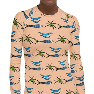 Puede incluir: Una camisa de manga larga de color melocotón con un patrón repetido de peces azules, palmeras verdes y olas azules.