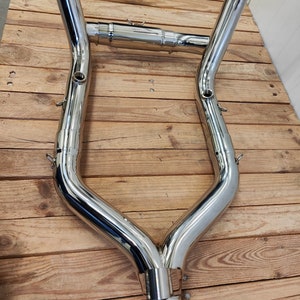 May include: A pair of polished chrome motorcycle exhaust pipes with a Y-shaped connector. The pipes are designed to fit together and are ready for installation.