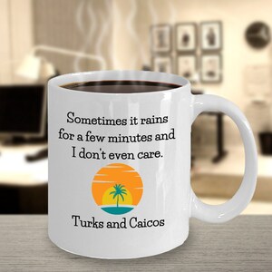 Peut inclure: Une tasse à café en céramique blanche avec un bord et une poignée noirs. La tasse présente un graphique d'un coucher de soleil avec un palmier et le texte "Sometimes it rains for a few minutes and I don't even care. Turks and Caicos".