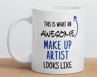 Può includere: Una tazza in ceramica bianca con un design nero e blu. Il testo sulla tazza recita "This is what an awesome make up artist looks like".