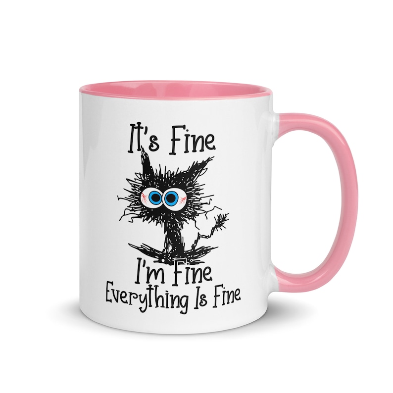 May include: White ceramic mug with a pink rim and handle. The mug features a black and white illustration of a cat with the text "It's Fine I'm Fine Everything Is Fine."