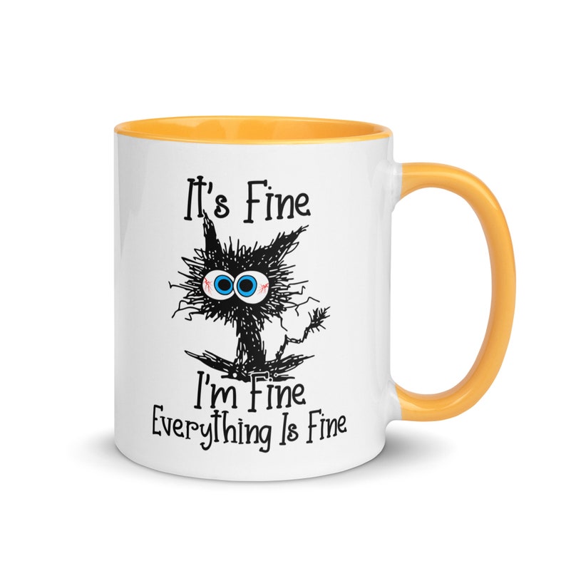 May include: White ceramic mug with a yellow rim and handle. The mug features a black and white illustration of a cat with the text "It's Fine I'm Fine Everything Is Fine."