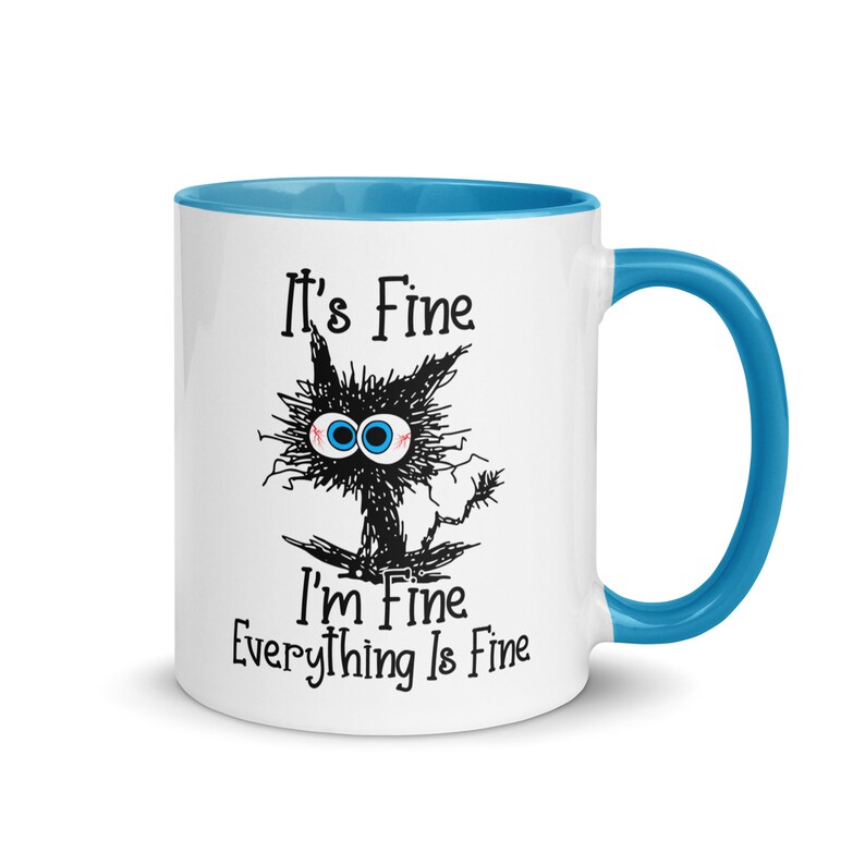May include: White ceramic mug with a blue rim and handle. The mug features a black and white cartoon cat with the text "It's Fine I'm Fine Everything Is Fine."