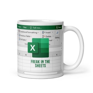 May include: White ceramic mug featuring a green and white design of the Microsoft Excel logo and the text "FREAK IN THE SHEETS".