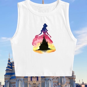 May include: White sleeveless crop top with a watercolor silhouette of a princess with a castle in her dress. The castle is black and the dress is a gradient of pink, orange, and yellow.