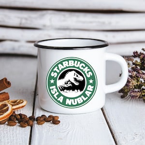 May include: White enamel mug with a black rim and handle. The mug features a green and white logo that reads "Starbucks Isla Nublar" with a black silhouette of a dinosaur inside the logo.