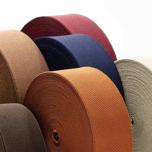 Könnte beinhalten: Sortiment aus sieben Gummibändern in verschiedenen Farben, darunter Braun, Beige, Marineblau und Rot. Die Bänder sind aufgerollt und in einem Halbkreis angeordnet.