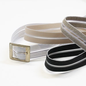 Può includere: Tre bande elastiche con una fibbia dorata. Le bande sono a righe bianche e beige, bianche e nere e beige.