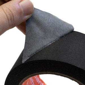 May include: A roll of black fabric tape with a grey fabric backing. The tape is being peeled back to reveal the adhesive.