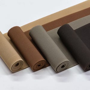 May include: Four rolls of elastic fabric in different shades of brown, beige, and grey. The fabric is rolled up and the ends are visible.