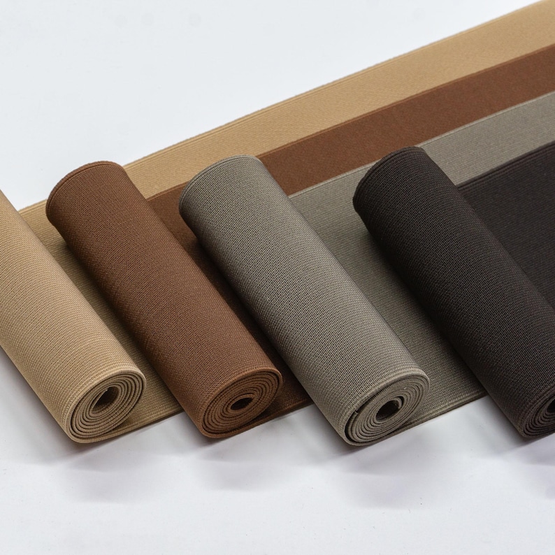 May include: Four rolls of elastic fabric in different shades of brown, beige, and grey. The fabric is rolled up and the ends are visible.