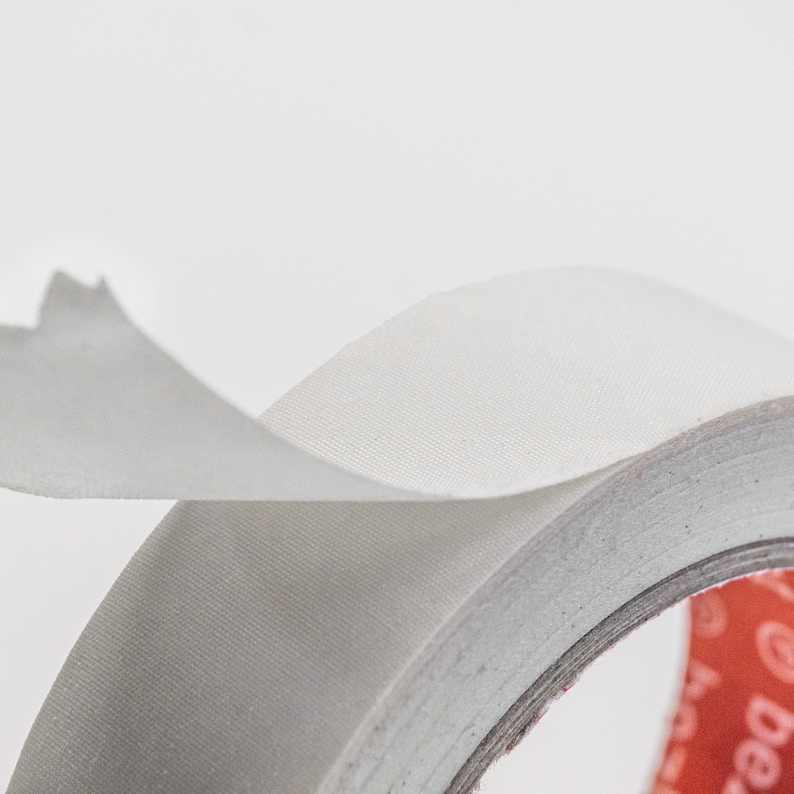 May include: A roll of white fabric tape with a red and white label. The tape is partially unrolled, showing the fabric texture.