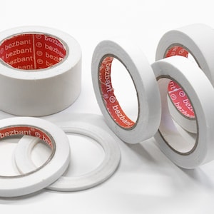 May include: Four rolls of white tape with red text that reads "bezbant" on the tape dispenser. The tape is on a white surface.
