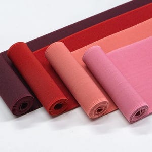 May include: Four rolls of elastic fabric in different shades of red, pink, and burgundy. The fabric is rolled up and the ends are visible.