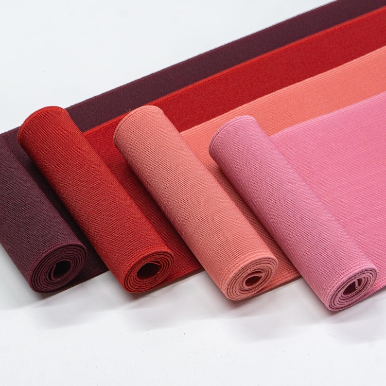 May include: Four rolls of elastic fabric in different shades of red, pink, and burgundy. The fabric is rolled up and the ends are visible.