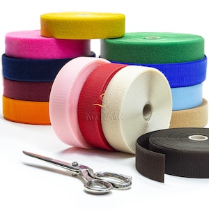 Puede incluir: Una colección de rollos de cierre de velcro de colores, incluyendo amarillo, rosa, verde y azul. Unas tijeras plateadas están en primer plano. La palabra "KEERMAN" es visible en los rollos. Medidas no visibles.