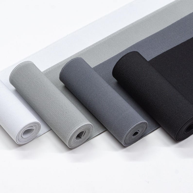 May include: Four rolls of elastic fabric in white, light grey, dark grey, and black. The fabric is rolled up and the ends are visible.