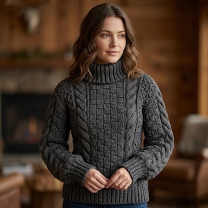 May include: A charcoal gray long-sleeve sweater featuring a high turtleneck collar, ribbed cuffs, and a ribbed hem. The garment displays a textured knit pattern with vertical cable knit columns on the sides and a central basketweave design.