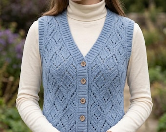 May include: A light blue knit vest featuring a V-neckline, a button-down front with five circular buttons, and a repeating diamond-shaped openwork pattern. The vest is layered over a cream-colored long-sleeve shirt with a high turtleneck collar.