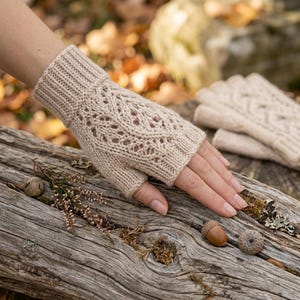 May include: A pair of beige fingerless gloves featuring a ribbed cuff and an intricate openwork lace pattern on the back of the hand. The gloves are knitted with a soft yarn and extend from the wrist to the base of the fingers.