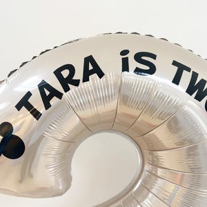 May include: Silver foil number two balloon with the text "TARA is TWO" in black. A black Mickey Mouse head is on the left side of the balloon. Perfect for a second birthday party.