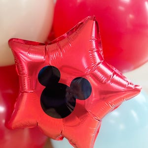 May include: A red star-shaped balloon with a black Mickey Mouse silhouette. The balloon is surrounded by other balloons in red, white, and light blue. This festive balloon is perfect for a birthday party or other celebration.