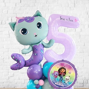 May include: A colourful balloon display with a mermaid cat character, a large number 5 balloon, and a Gabby's Dollhouse balloon. The balloons are in blue, purple, and pink, ideal for a birthday party. The number 5 balloon has the text "Tara is Five".