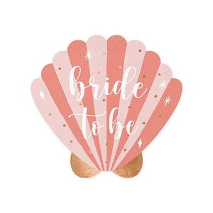 Peut inclure: Une serviette en papier en forme de coquillage corail et rose clair, avec des accents dorés. Les mots "bride to be" sont écrits en script blanc au centre. La base de la coquille est de couleur or métallique.