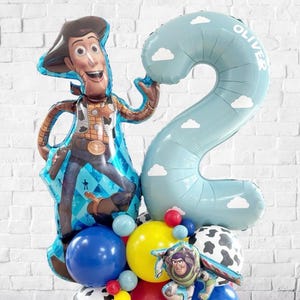 Puede incluir: Un arreglo festivo de globos con un gran globo del personaje Woody y un globo azul claro con el n&uacute;mero 2 y el nombre "Oliver". El arreglo incluye varios globos coloridos, incluyendo globos azules, amarillos, rojos y con estampado de vaca, ideal para una fiesta de cumplea&ntilde;os.