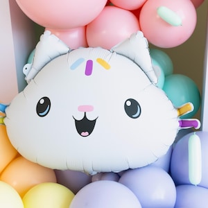 May include: A white cat-shaped balloon with black eyes, a pink nose, and a smiling mouth, surrounded by pastel-colored balloons. The balloon has colorful accents on its head and arms.