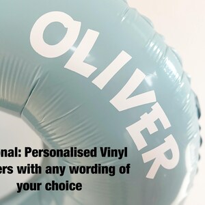 Puede incluir: Globo de papel de aluminio azul claro con el nombre "OLIVER" en letras may&uacute;sculas blancas grandes. El globo est&aacute; parcialmente inflado y tiene una superficie brillante. El texto en la parte inferior dice "Optional: Personalised Vinyl stickers with any wording of your choice."