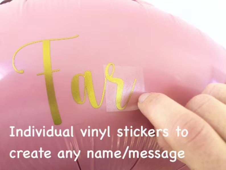 May include: A pink balloon with gold vinyl lettering spelling "Far". The image shows a hand applying a clear sticker with the gold lettering. The text "Individual vinyl stickers to create any name/message" is also visible.