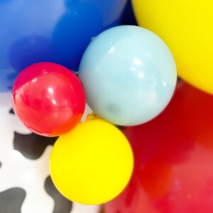 Puede incluir: Primer plano de globos coloridos en rojo, azul, amarillo y azul claro. Algunos globos son de colores lisos, mientras que otros tienen un estampado de vaca. Los globos est&aacute;n agrupados, creando un ambiente festivo y de celebraci&oacute;n.