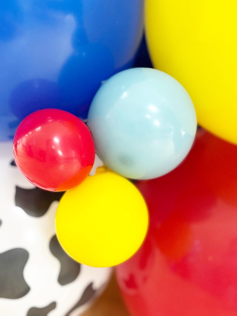 Puede incluir: Primer plano de globos coloridos en rojo, azul, amarillo y azul claro. Algunos globos son de colores lisos, mientras que otros tienen un estampado de vaca. Los globos est&aacute;n agrupados, creando un ambiente festivo y de celebraci&oacute;n.