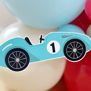 May include: A light blue race car sticker with black wheels and the number 1 on a white circle. The sticker is set against a backdrop of white, light blue, and red balloons, creating a festive atmosphere.